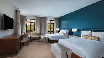 A hotel room with a large bed, a smaller bed, a desk, a chair, a sofa, and a TV.