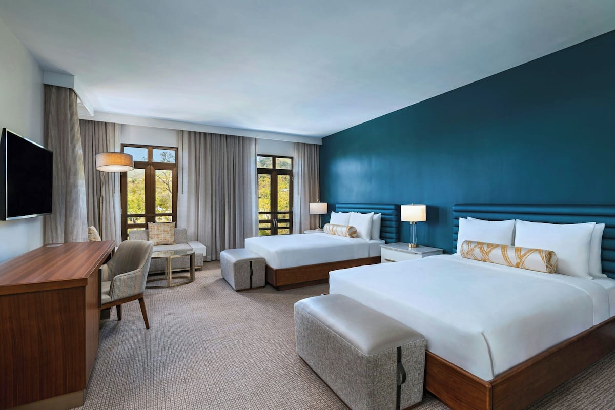 A hotel room with a large bed, a smaller bed, a desk, a chair, a sofa, and a TV.