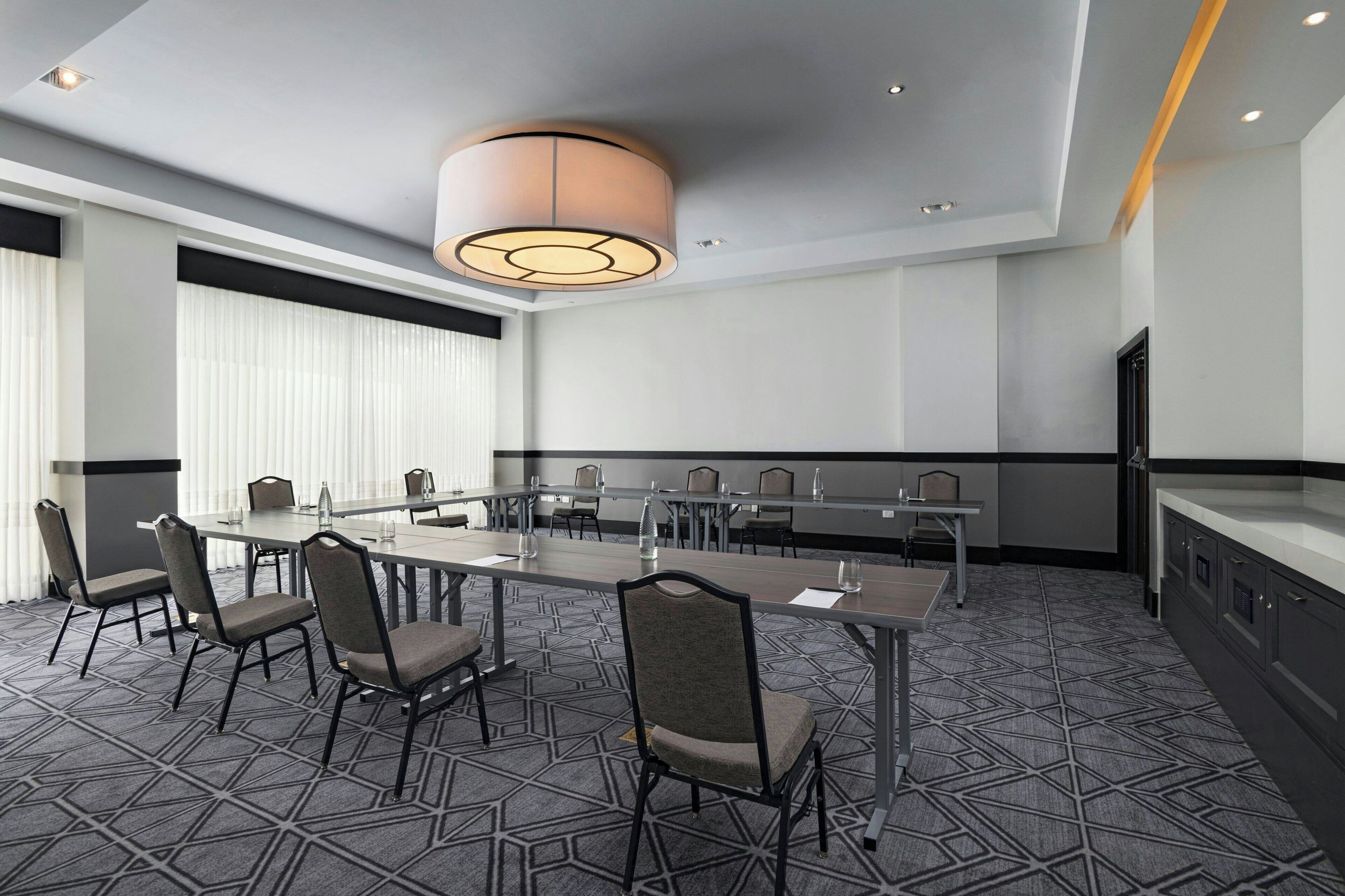 A conference room with a long table, chairs, a modern pendant light, and a patterned carpet.