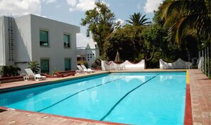 A swimming pool with lounge chairs and a modern building in the background. - Los Olivos Spa (Oaxaca)