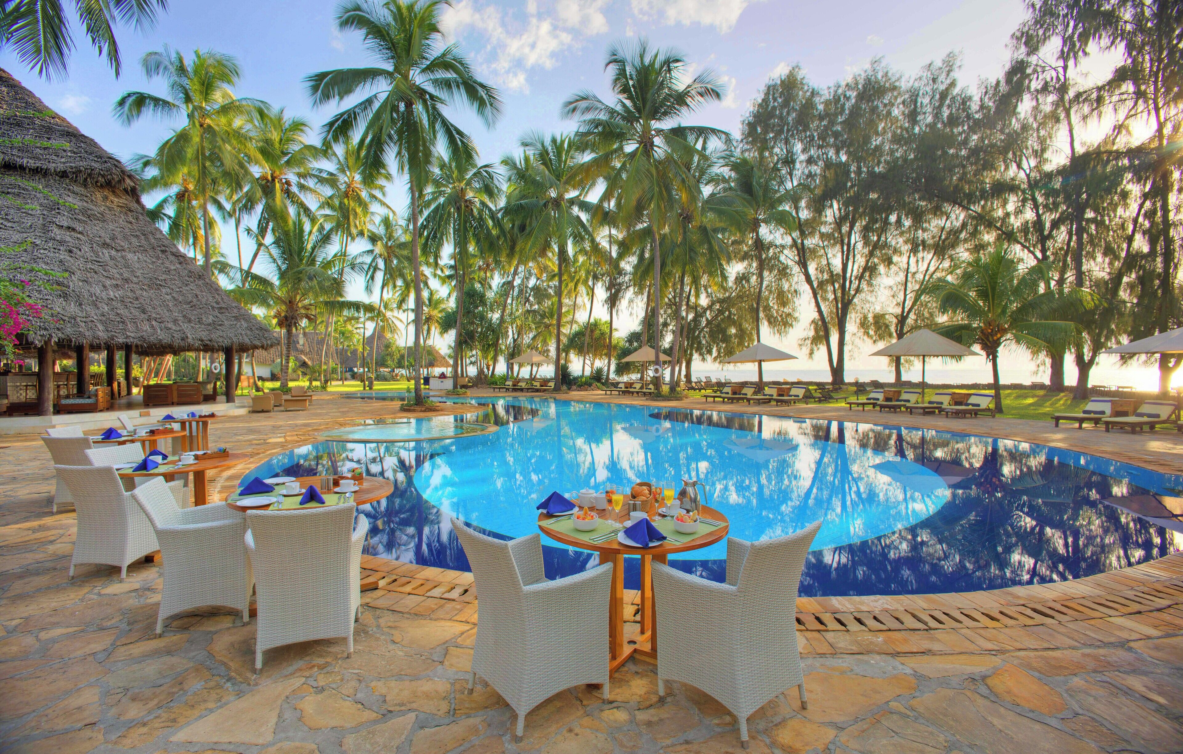 A poolside area with lounge chairs, a dining table with a meal set, and a thatched-roof structure.