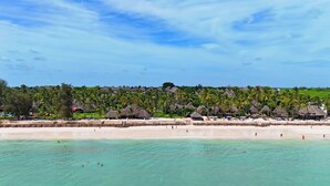 A beach resort with thatched-roof bungalows, a sandy beach, and clear turquoise waters. - Bluebay Beach Resort & Spa (Kiwengwa)