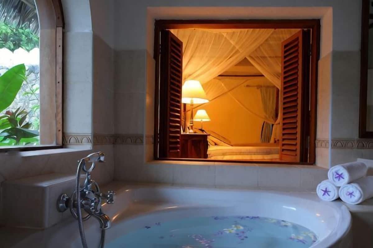 A bathroom with a bathtub, a window with curtains, and a towel rack.