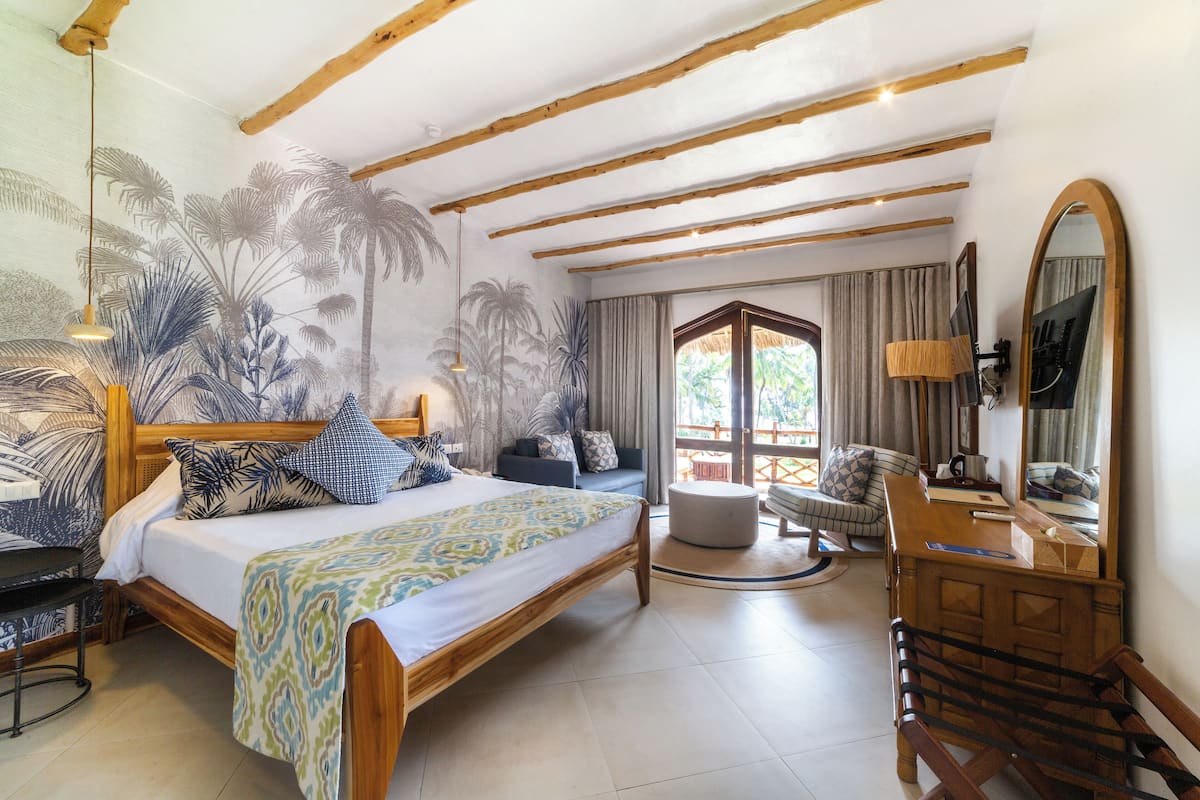 A bedroom with a bed, a chair, a desk, a mirror, and a mural of palm trees.