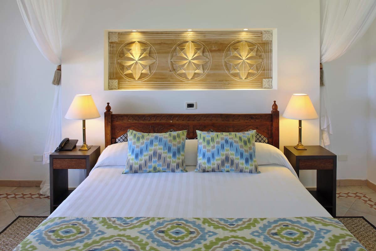 A hotel room with a large bed, two bedside lamps, a decorative wall piece, and a patterned rug.