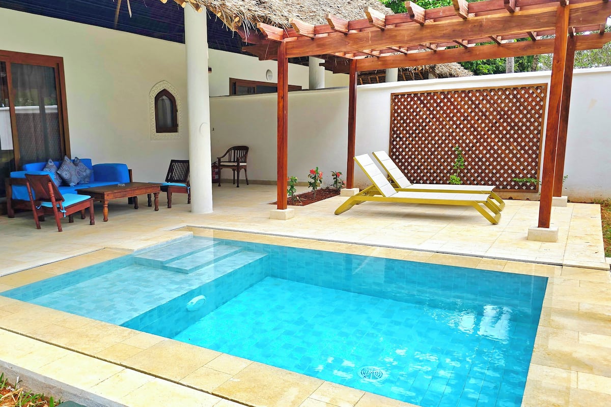 A swimming pool with a pergola and lounge chairs, a blue sofa, and a wooden table.