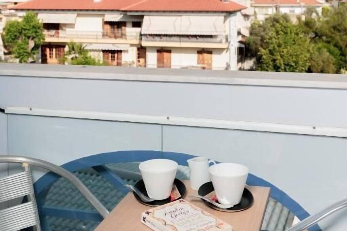 A balcony with a table set for two, overlooking a hillside with buildings.