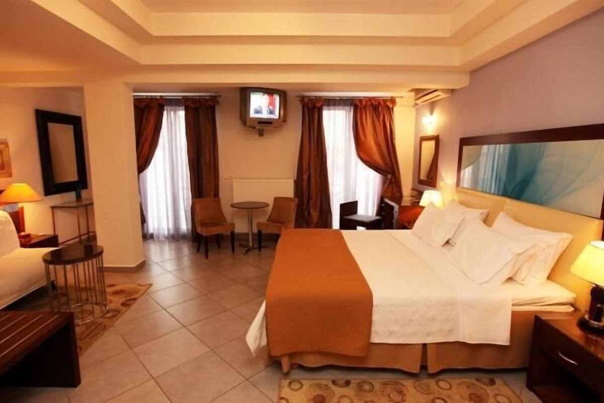 A hotel room with a bed, a desk, a chair, a TV, and a painting on the wall.