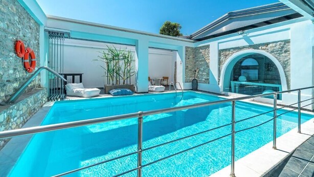 Une piscine intérieure moderne, avec une eau d’un bleu limpide, des murs en pierre et un espace clos par des parois de verre.