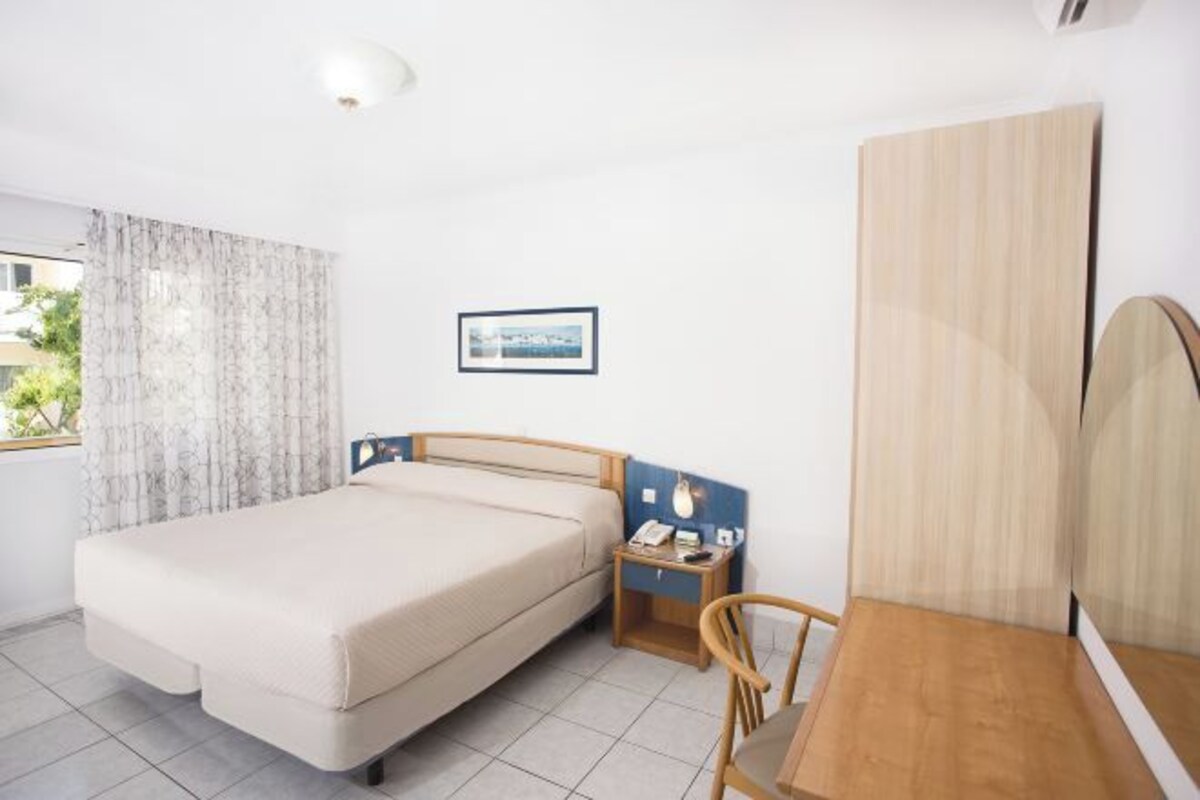 Quarto com cama, mesa de cabeceira, cadeira e janela com cortinas.