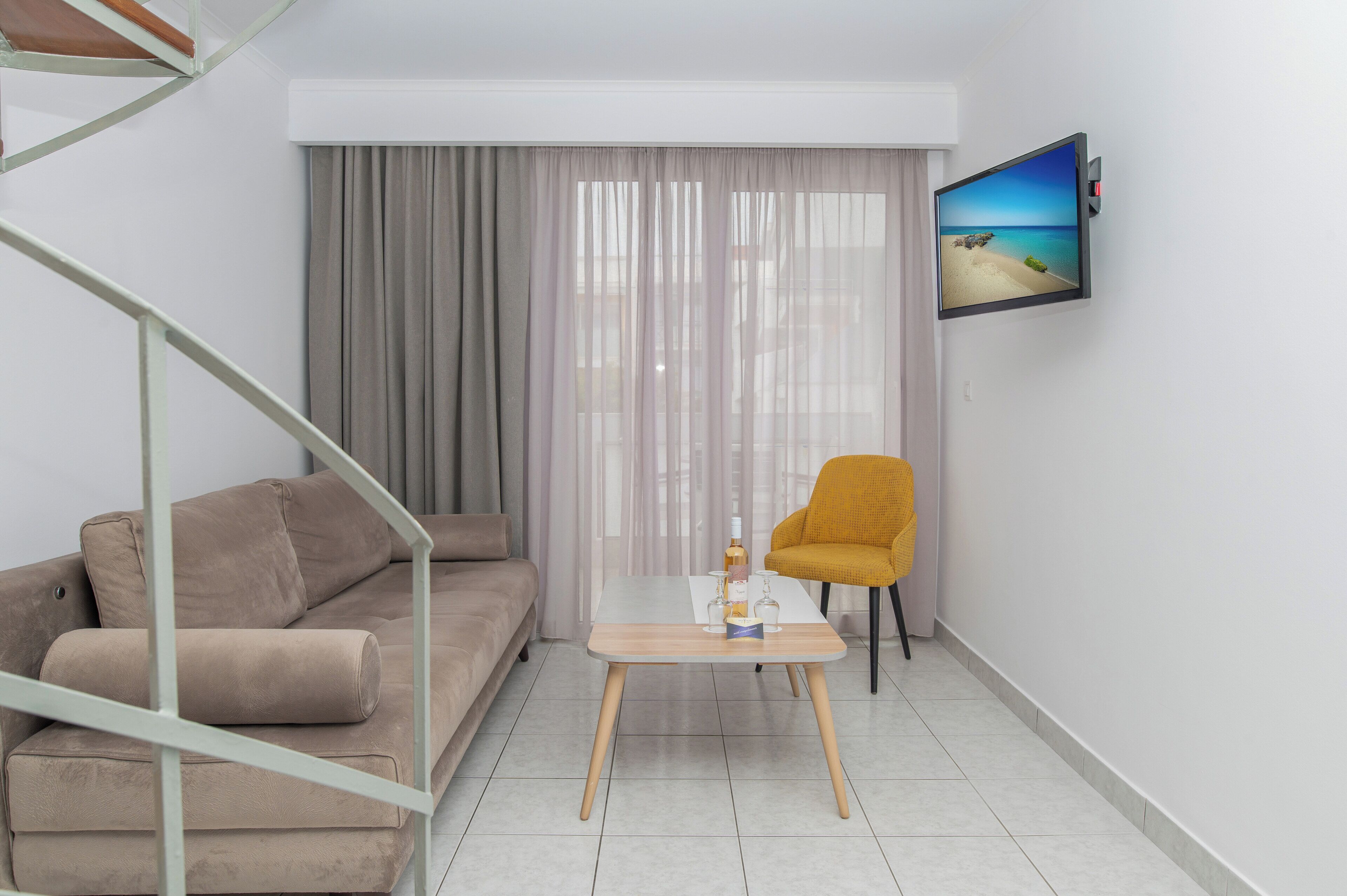 Ein modernes Wohnzimmer mit einer Couch, einem kleinen Tisch mit einer Flasche, einem Sessel, einem an der Wand befestigten Fernseher und einer Treppe.