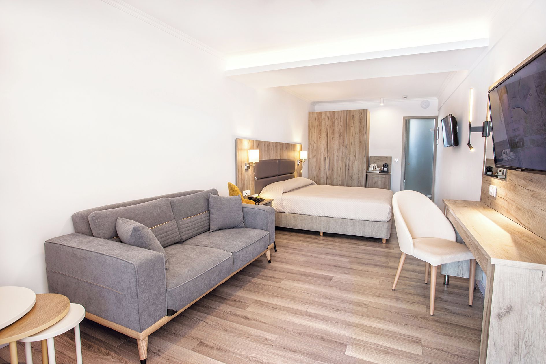 Una habitación de hotel moderna con sofá gris, cama, escritorio y televisión.