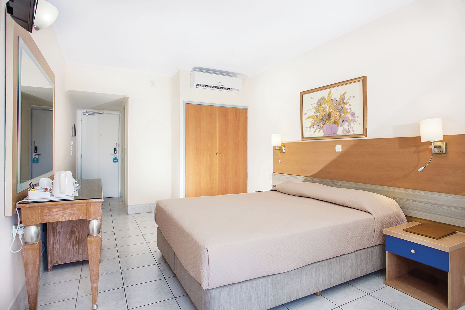 A hotel room with a bed, bedside table, lamp, and a painting on the wall.