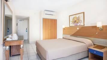 A hotel room with a bed, bedside table, lamp, and a painting on the wall.