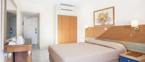 A hotel room with a bed, bedside table, lamp, and a painting on the wall.