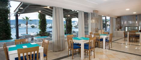Un restaurante con terraza al aire libre que da a un puerto deportivo, con piso de baldosas y sillas de madera.