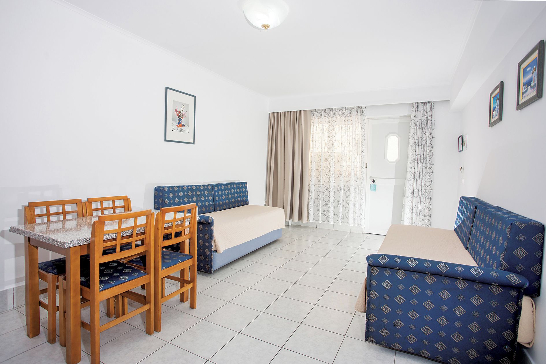 A room with a bed, a sofa, a dining table with chairs, and a small window with curtains.
