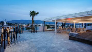 A rooftop terrace with outdoor seating, a view of the city, and a palm tree.