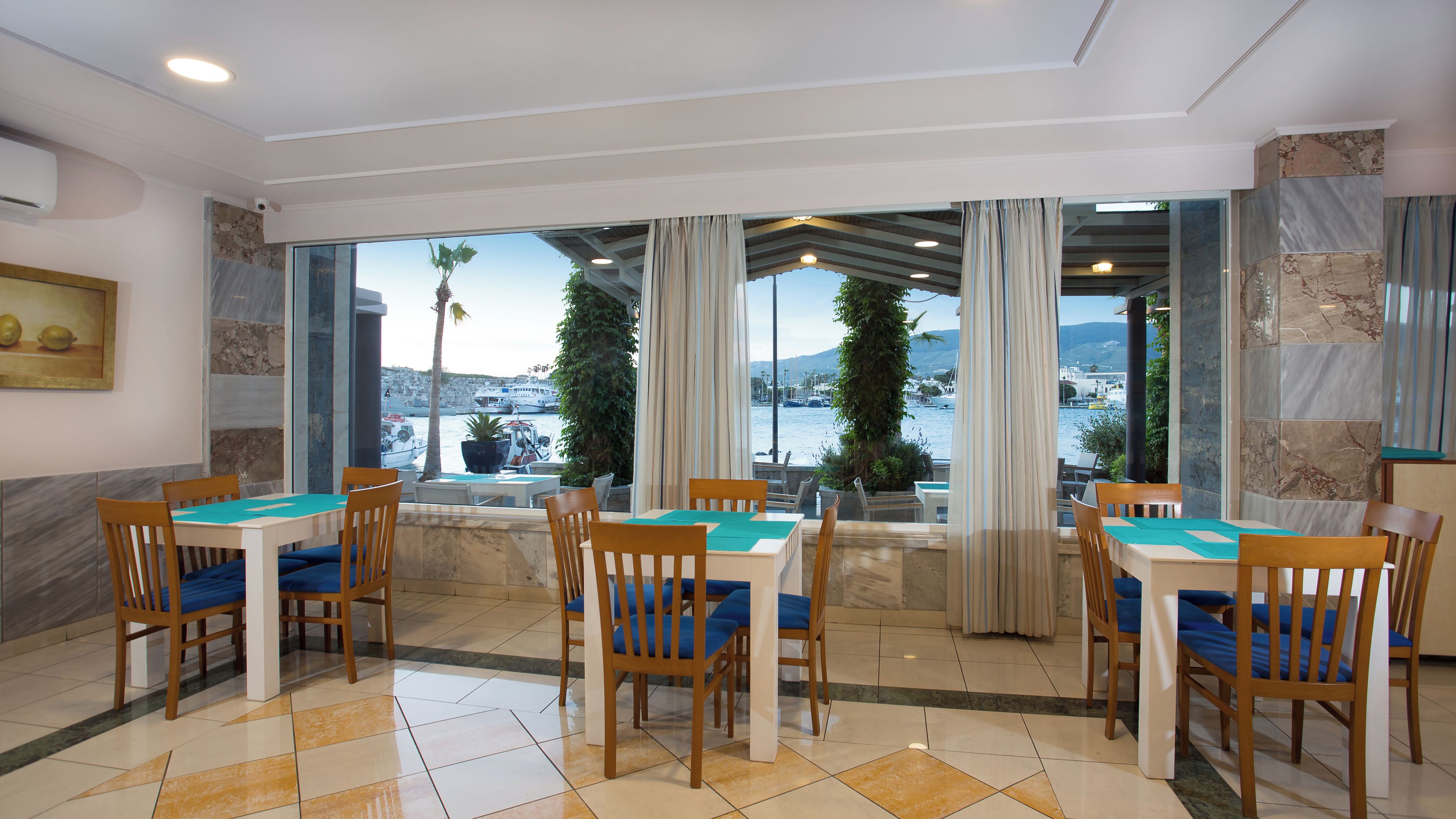 Un comedor con vistas al mar, con una mesa, sillas, una planta en maceta y un cuadro en la pared.