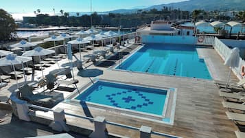 A pool area with multiple sun loungers and umbrellas, a no diving sign, and a view of the sea and mountains in the background.