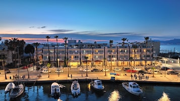 A waterfront hotel with multiple balconies, a marina with boats, and a view of the sea.
