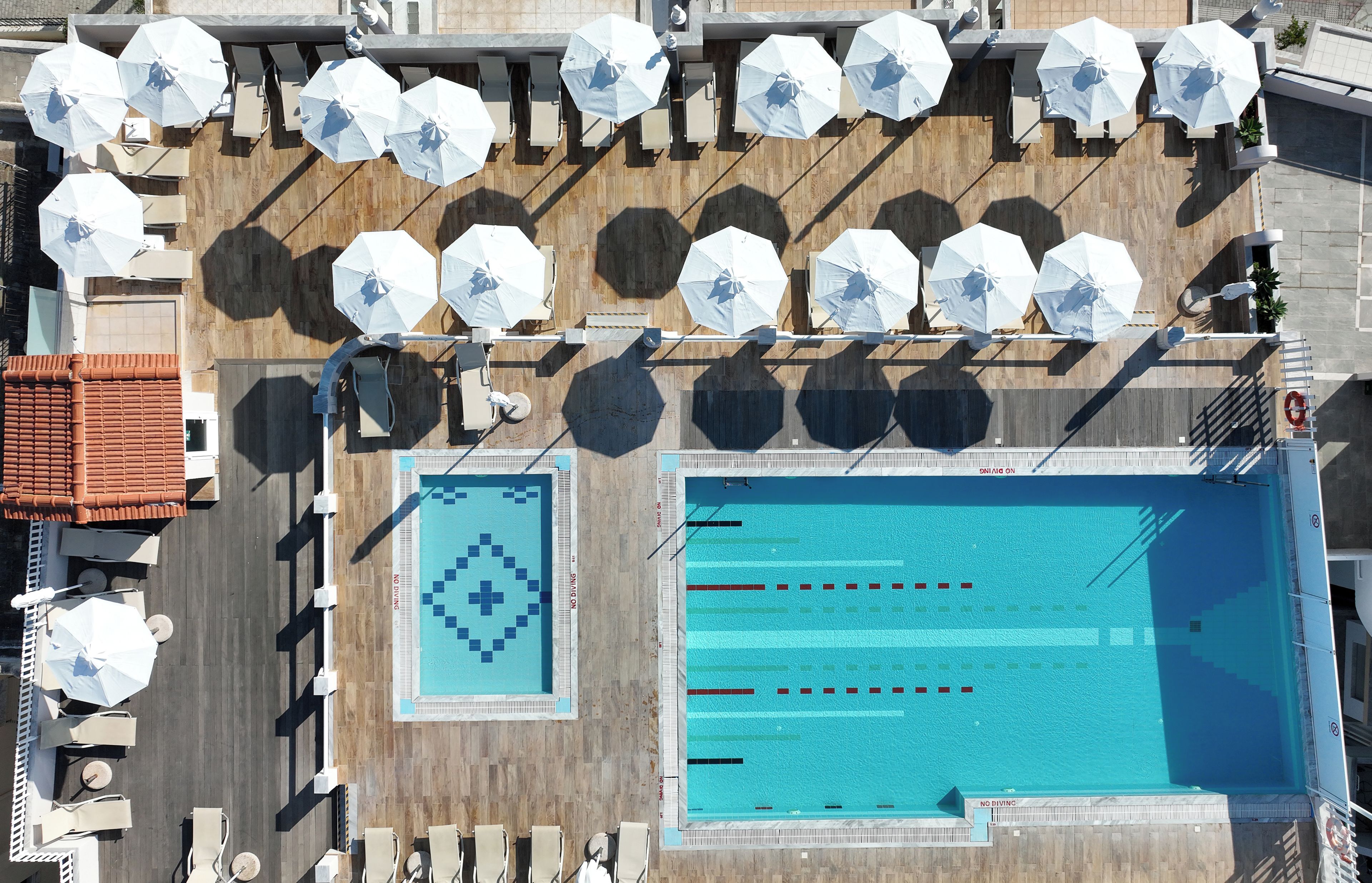 A rooftop pool area with multiple sun umbrellas, lounge chairs, and a swimming pool with lane markers.