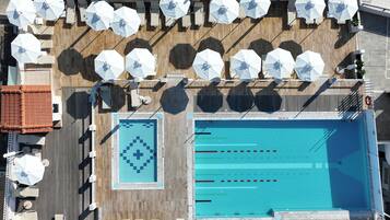 A rooftop pool area with multiple sun umbrellas, lounge chairs, and a swimming pool with lane markers.