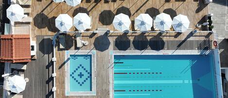 A rooftop pool area with multiple sun umbrellas, lounge chairs, and a swimming pool with lane markers.