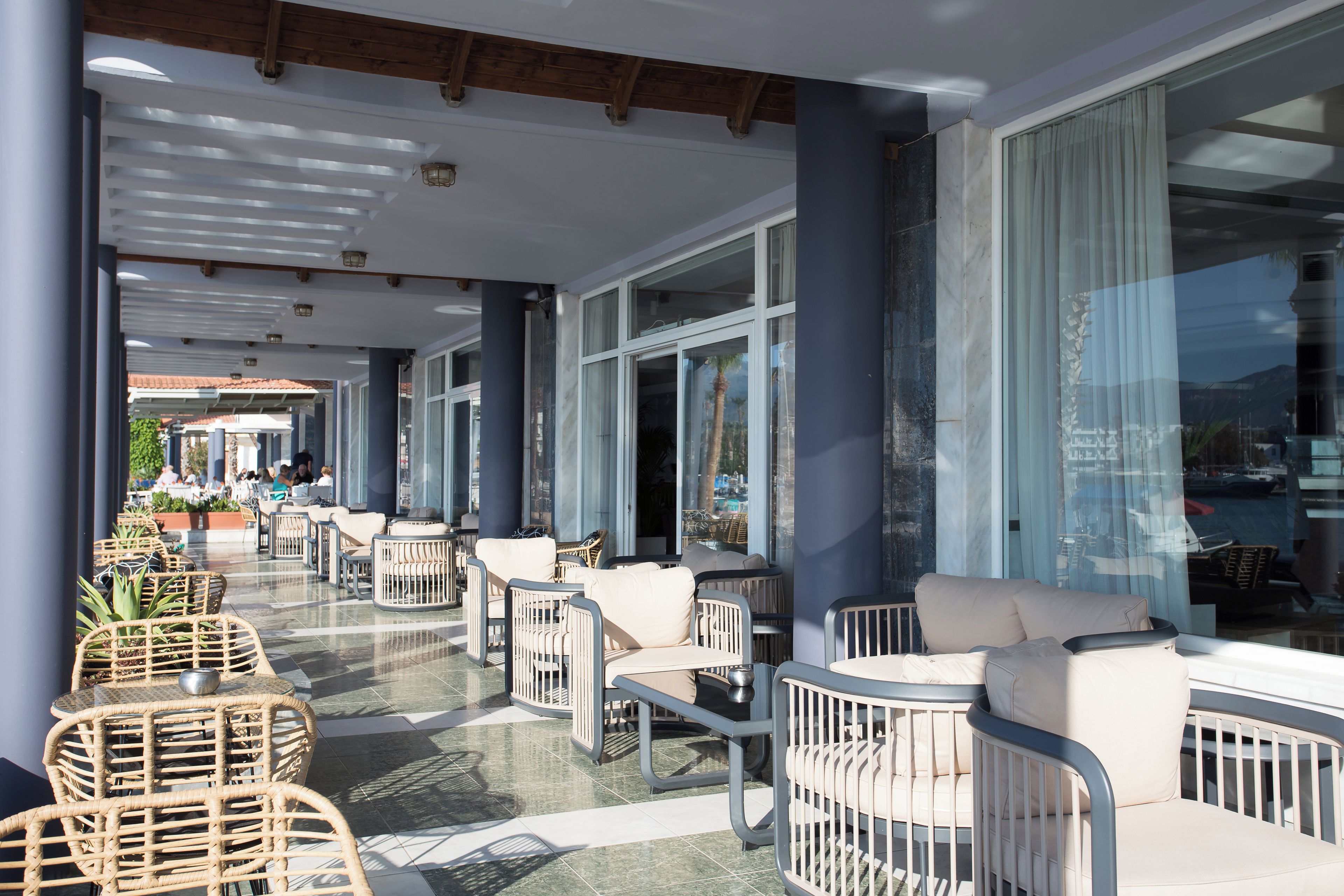 Een terras met rieten stoelen en tafels, grote ramen en uitzicht op de straat.