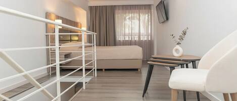 Una habitación de hotel moderna con cama, televisor, escritorio con silla y una mesita con florero.