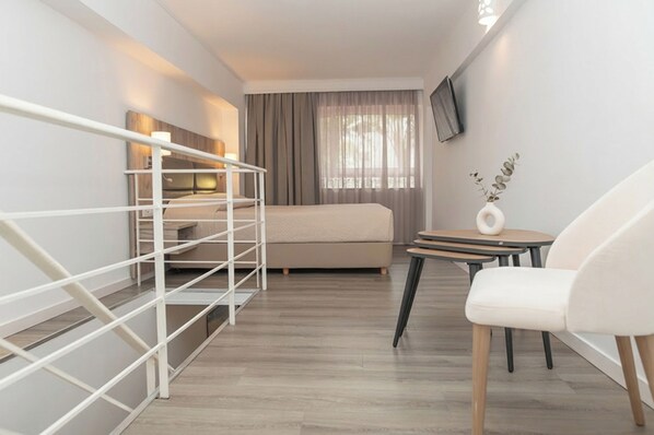 A modern hotel room with a bed, a TV, a desk with a chair, and a small table with a vase. - Kosta Palace (Kos)