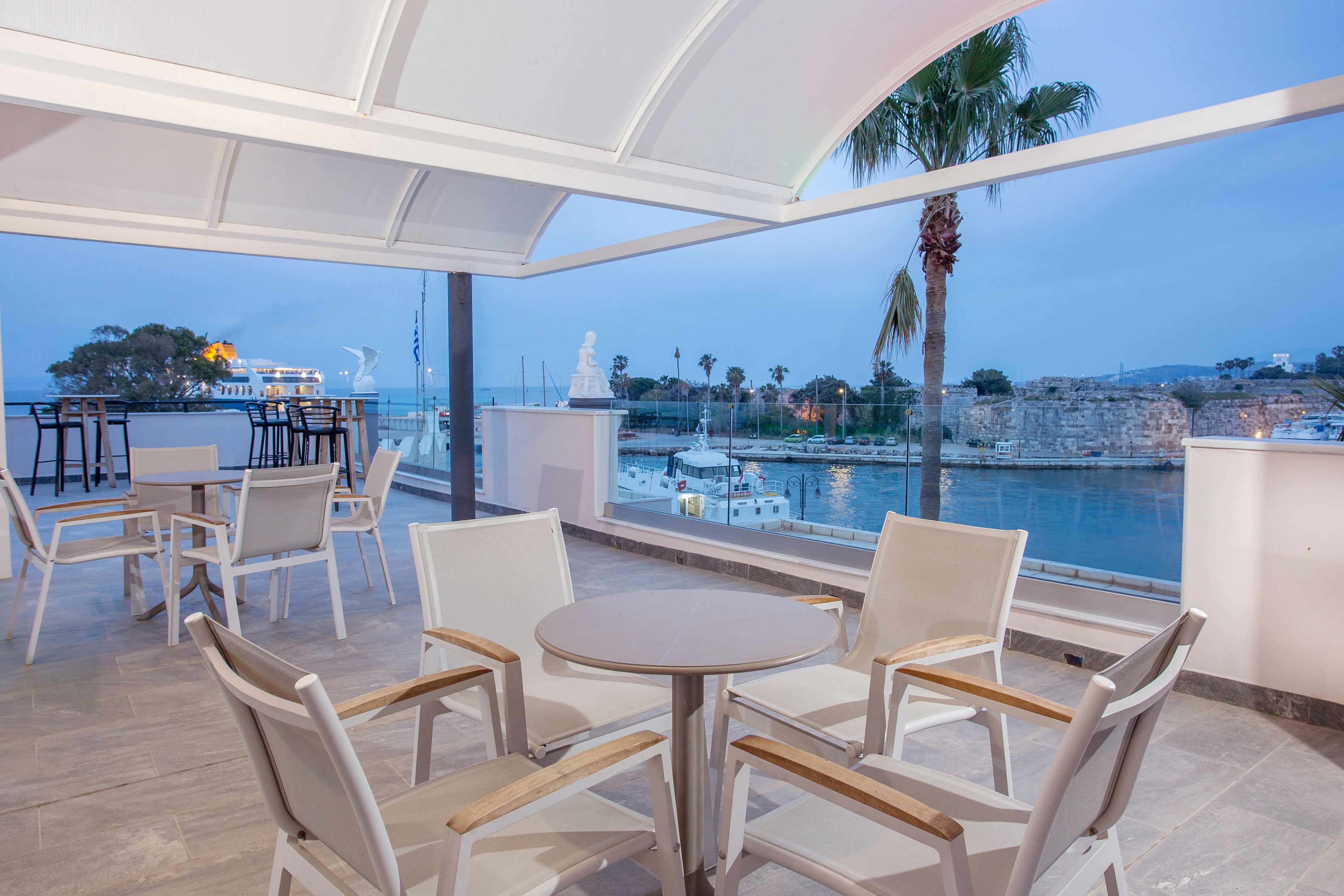 Eine Terrasse mit weißen Möbeln, Blick auf das Meer und einer Statue.