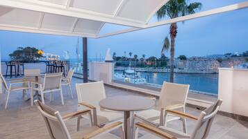 Eine Terrasse mit weißen Möbeln, Blick auf das Meer und einer Statue.