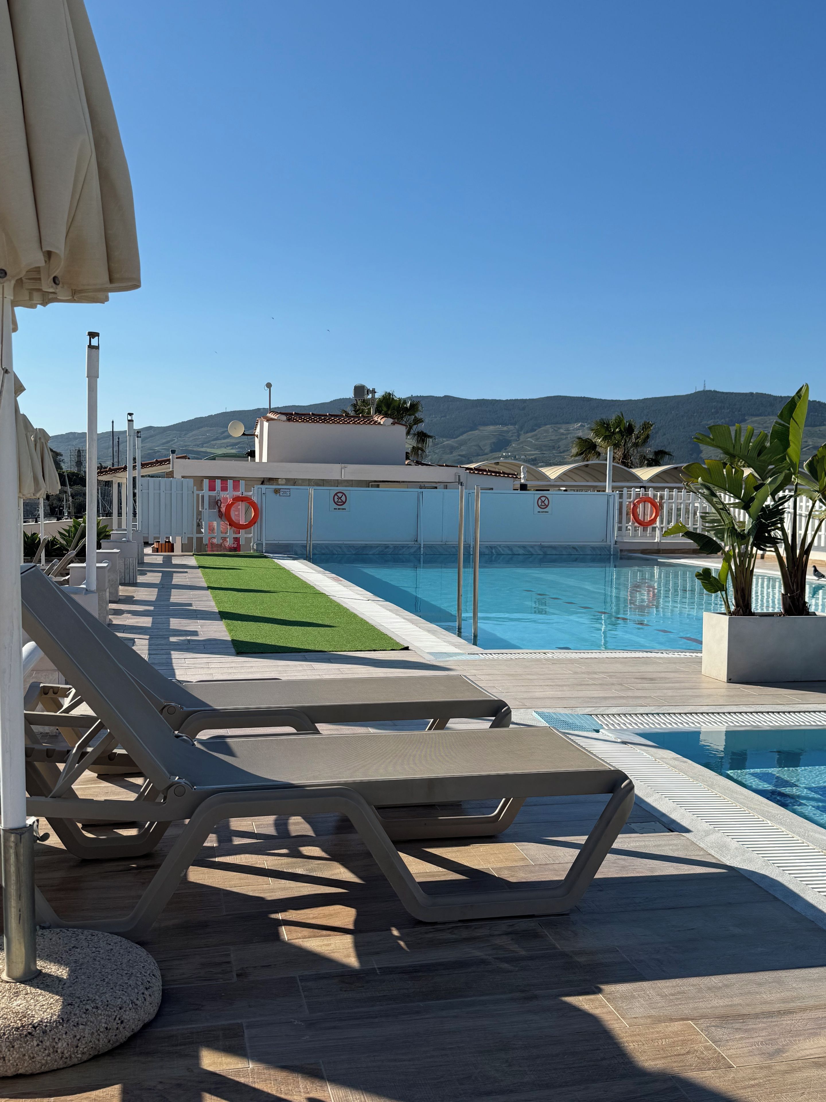 A poolside area with lounge chairs, a lifebuoy, and a view of hills.