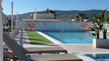 A poolside area with lounge chairs, a lifebuoy, and a view of hills.