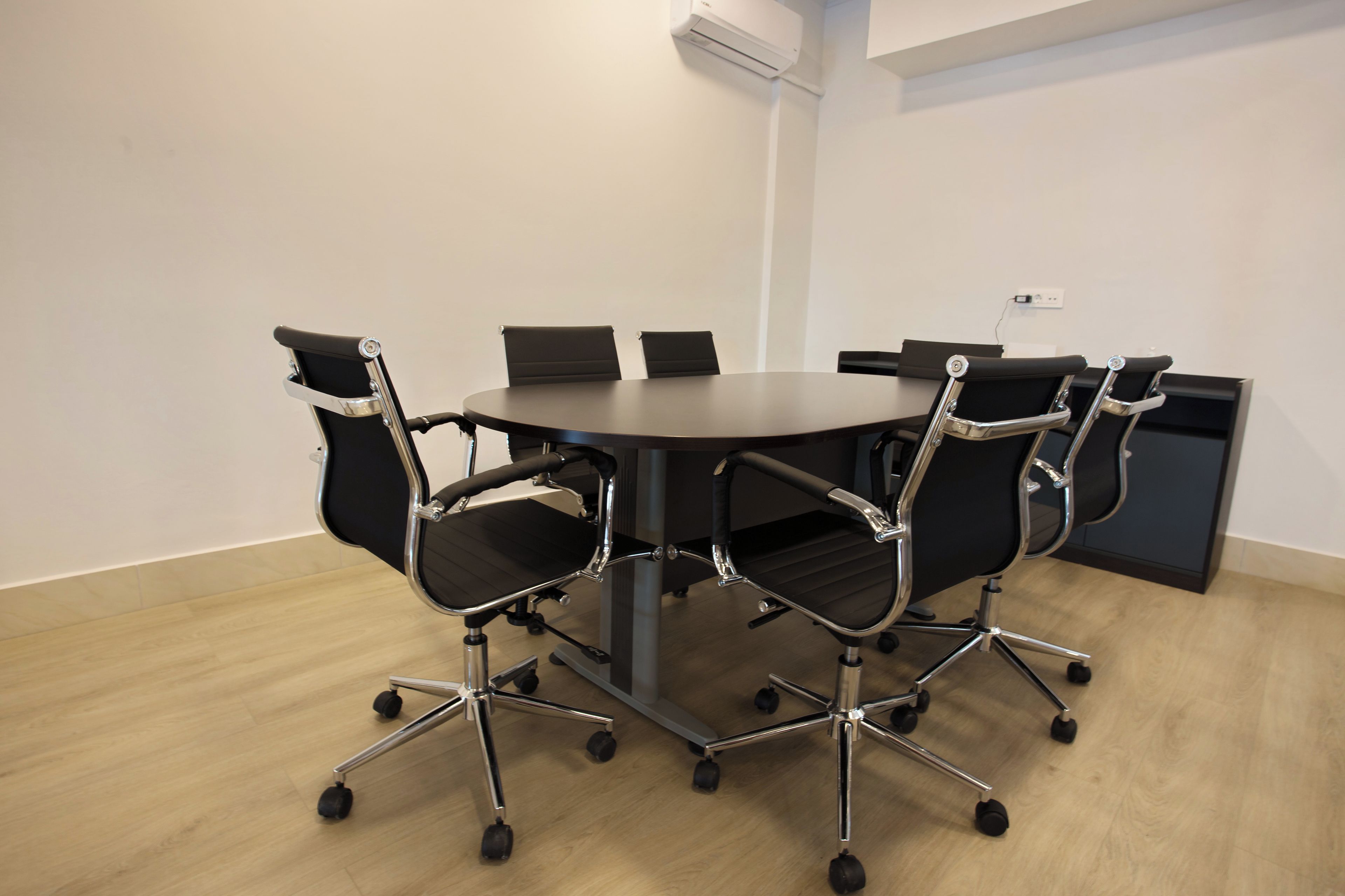 Un salón de conferencias con una mesa redonda y seis sillas de oficina con ruedas.