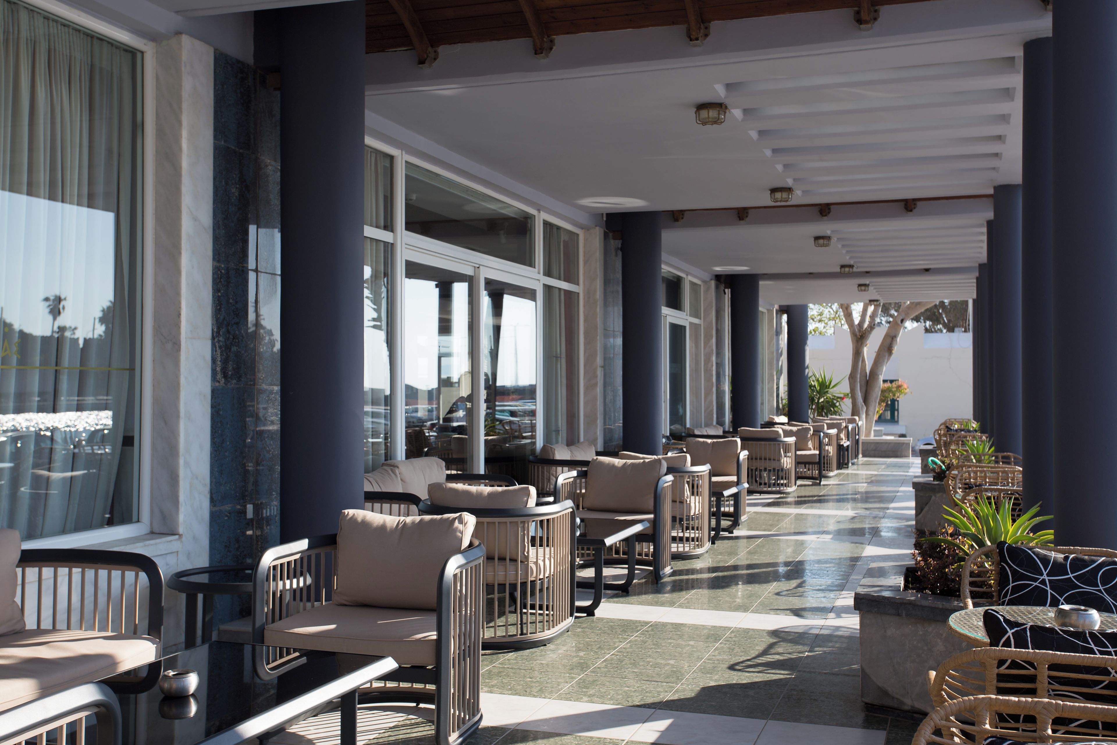 A covered outdoor seating area with tables and chairs, large windows, and a tiled floor.