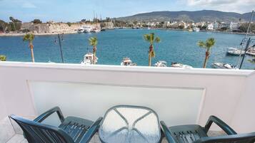 A balcony with two chairs and a table overlooking a marina with boats and a coastal town.