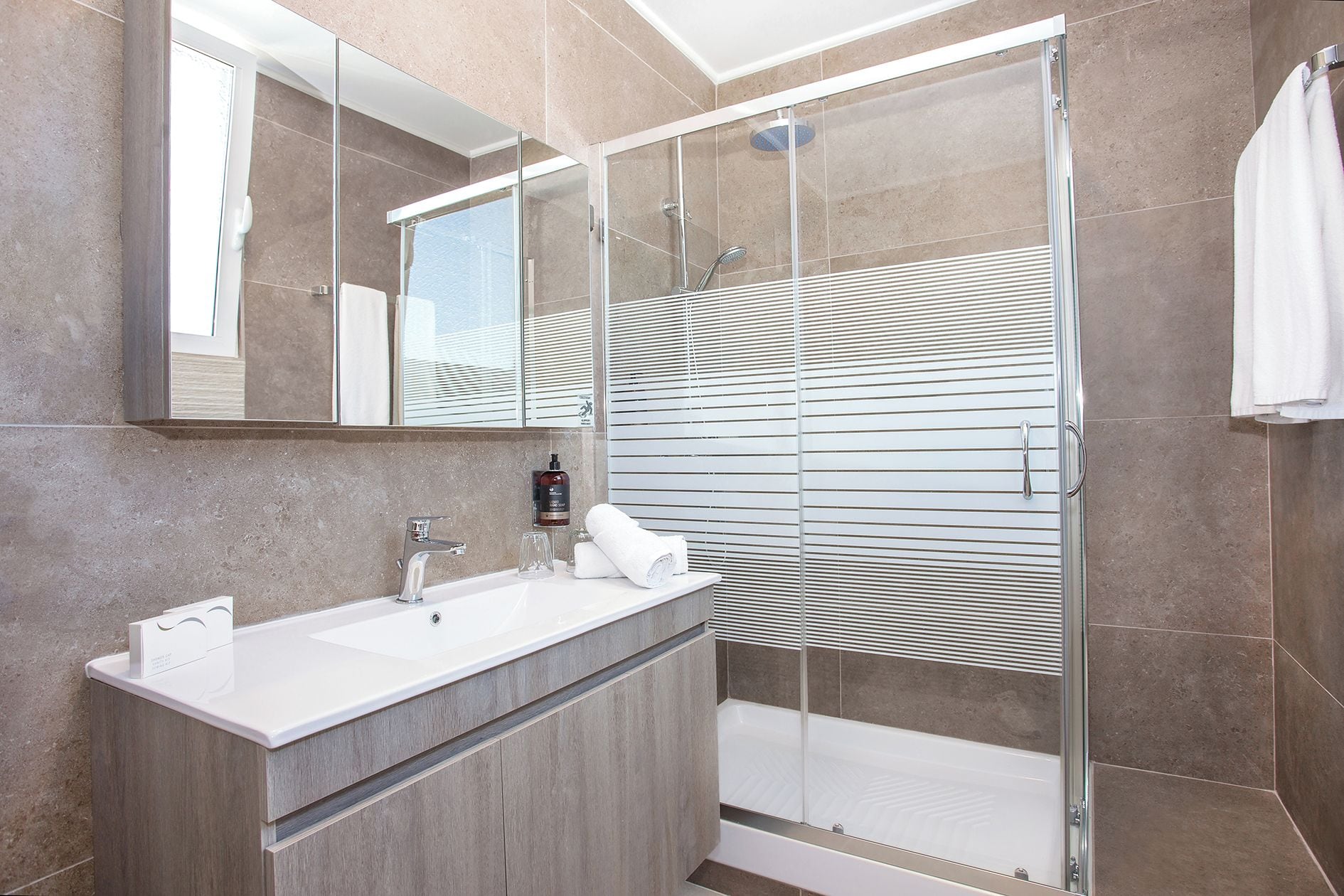A modern bathroom with a glass shower enclosure, a white sink, and a mirror.