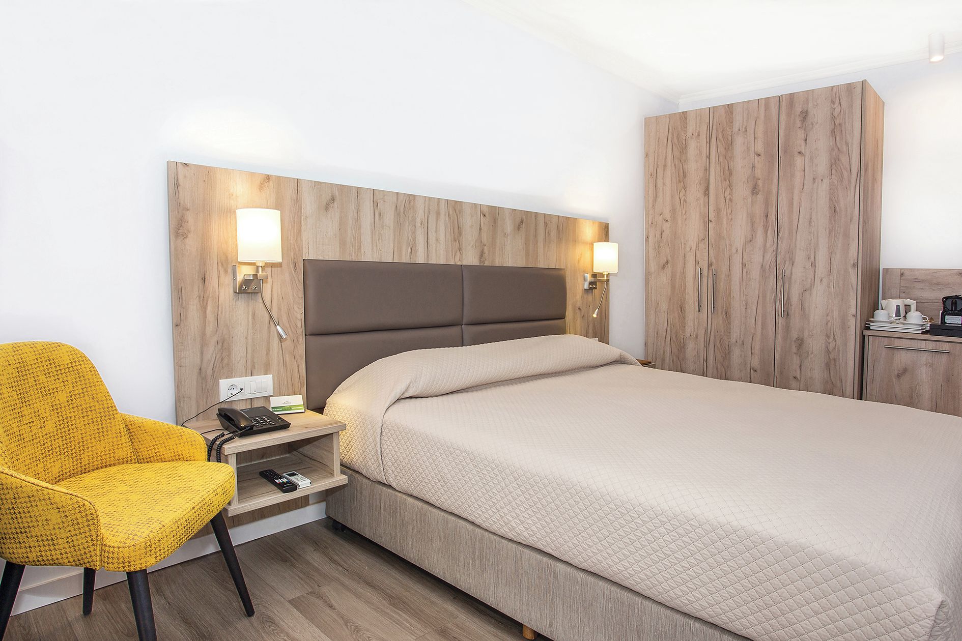 A hotel room with a bed, bedside table, lamp, chair, and wardrobe.