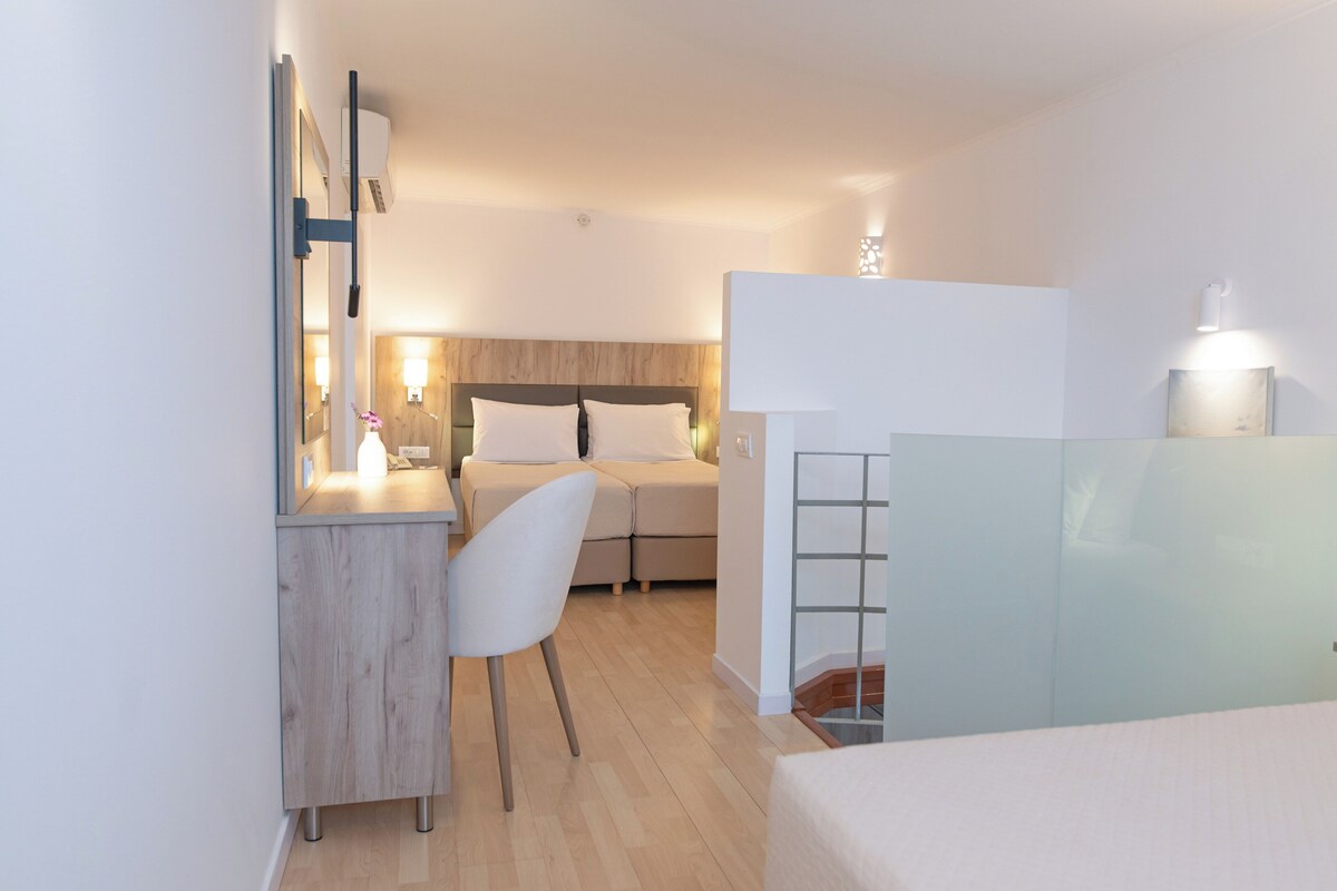 A modern hotel room with a bed, a desk, a chair, and a small table.