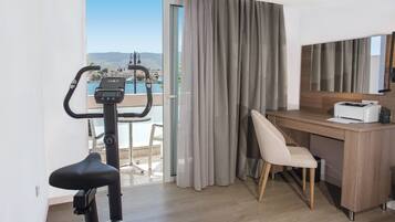 Quarto de hotel com escrivaninha, cadeira, bicicleta ergométrica e vista para o mar.