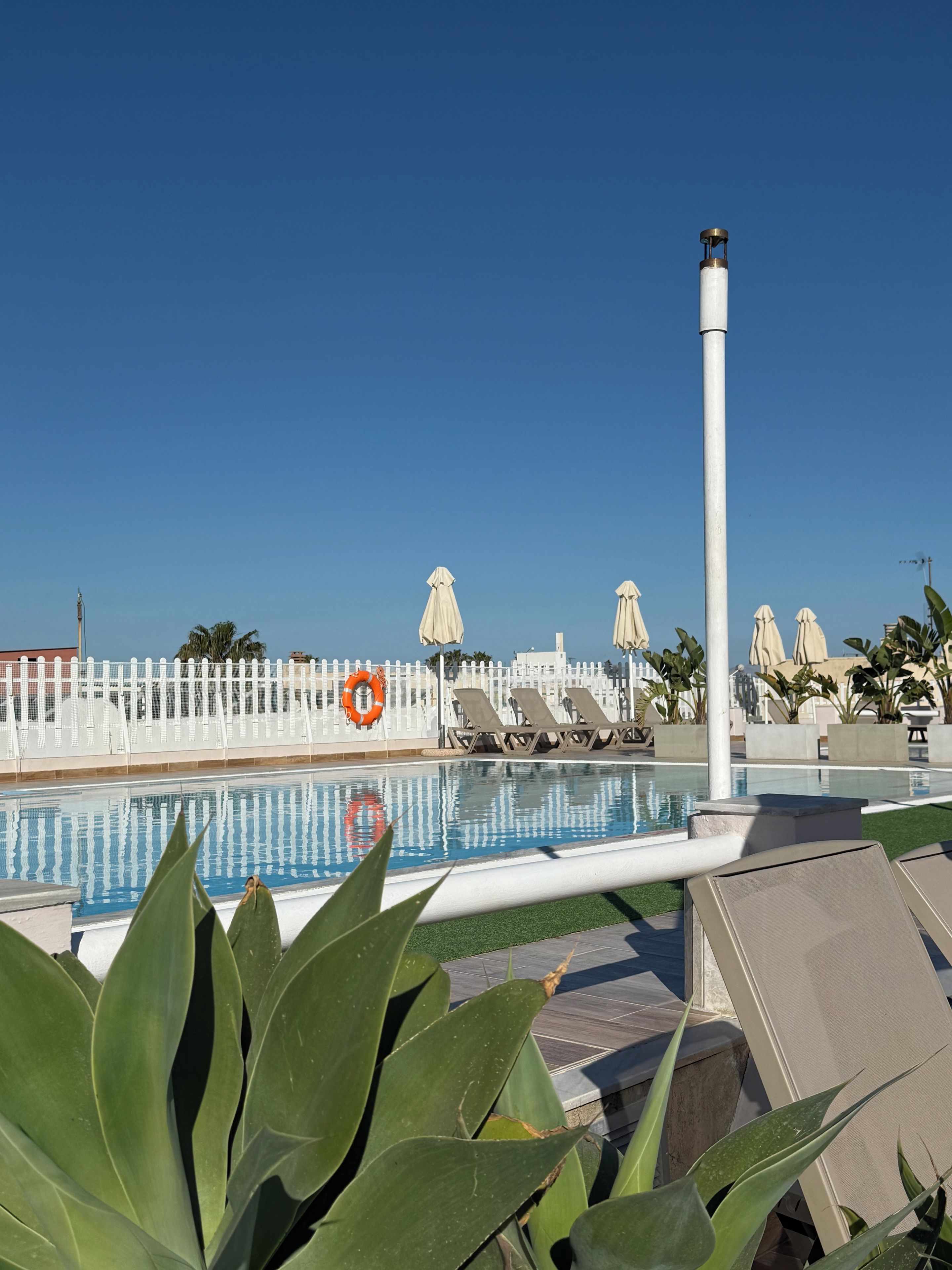 A pool area with lounge chairs, umbrellas, and a lifebuoy.
