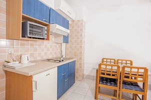 Cocina compacta con microondas, estufa y lavamanos, armarios azules y una pequeña zona de comedor con sillas de madera.