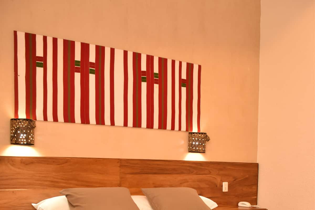 Una cama bien hecha con cabecera a rayas rojas y blancas, dos lámparas de noche y una mesita de madera.