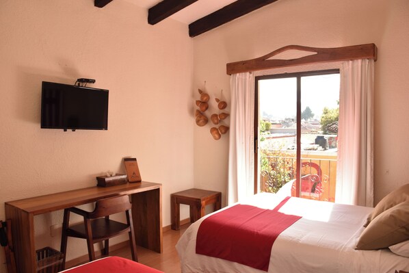 A bedroom with a bed, a desk, a chair, a television, and a balcony with a view.