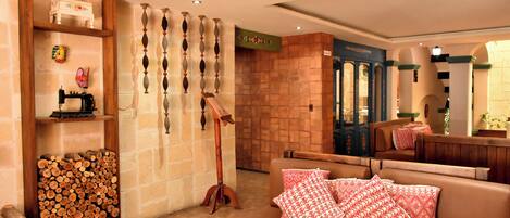Un hall con un sofá de cuero marrón, una pila de leña, una máquina de coser y una pared decorada con jarrones.