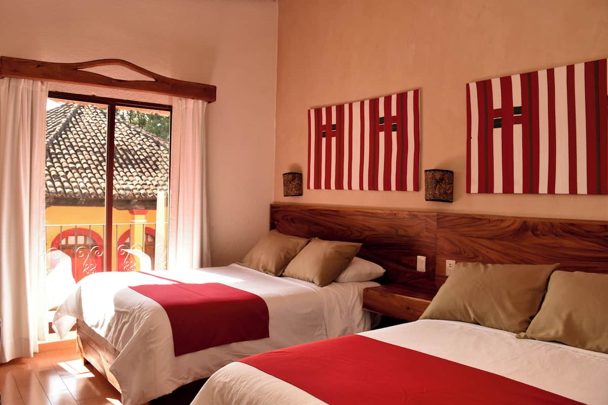 Habitación de hotel con dos camas, cabecera de madera y vista a un tejado de baldosas por una puerta corredera.