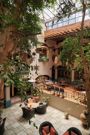 An indoor courtyard with wicker furniture, potted plants, and a tiled floor.