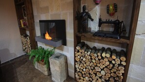 Una chimenea encendida, un montón de leña y una máquina de coser sobre un estante.